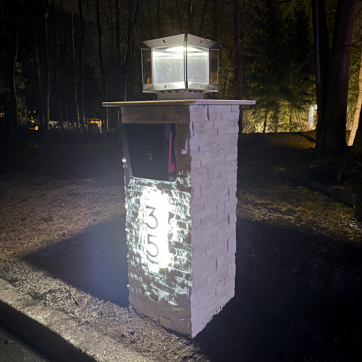 A white faux marble pillar mailbox installed at the end of a residential driveway