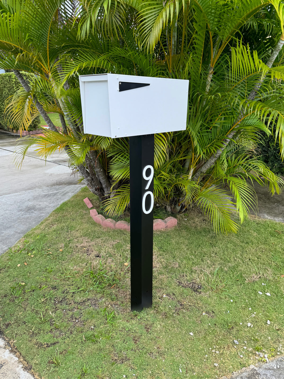 A dark, modern post-mounted mailbox with a locking door at the curb of a planned community home